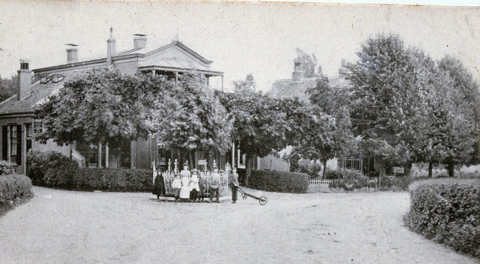 Het pand van de uitgever/boekhandelaar G. Romijn. Op de voorgrond een gezelschap rond de Wilhelmina-linde.