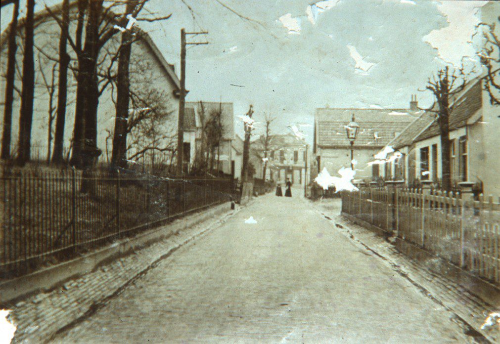 Weverstraat rond 1900 in noordelijke richting. Links het tuinhek van huis "Hoogerheide". Op de achtergrond het kort daarvoor door T.C. van Rijn betrokken pand, daarvoor enige tijd woonhuis van burgemeester Toulon van der Koog. Ook van Rijn kwam van de Beneden-Weverstraat.