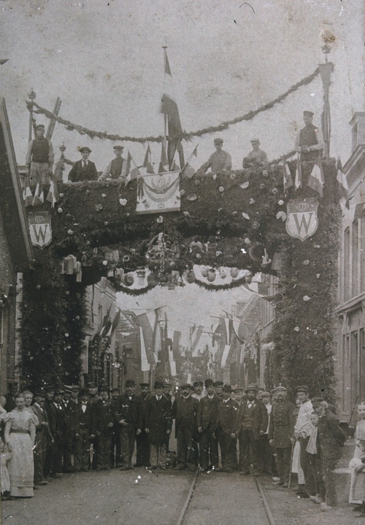 De Dorpsstraat met ereboog. Links achter de boog “Hotel Verwaaijen” Geheel links, nog net zichtbaar, een deel van het bierhuis van Panman, later het pand van de stalhouder Jan van Ee. We kijken oost- west.